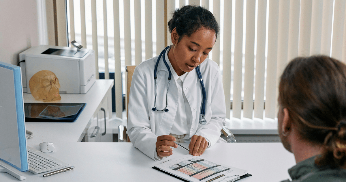 Doctor reviewing patient chart in office. Medical professional at desk with patient. Healthcare consultation.