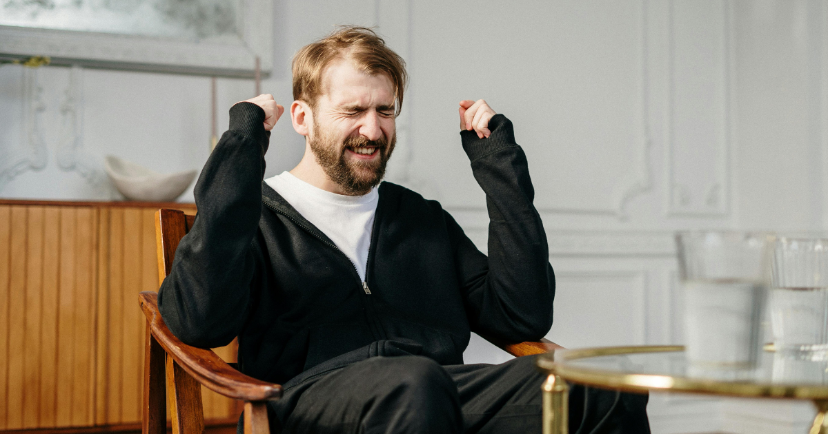 Jealousy vs Envy: Man in chair with fists clenched, expressing strong emotion, possibly envy or jealousy.