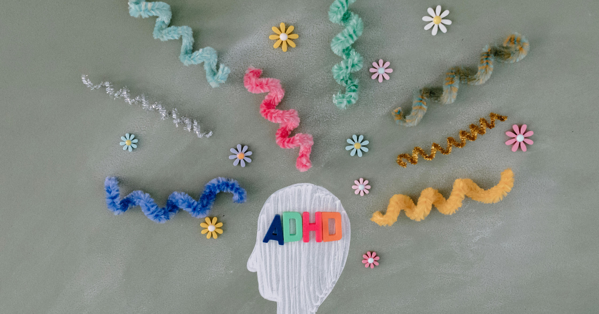 ADHD concept image: Head silhouette with ADHD letters, colorful pipe cleaners, and flower decorations. Mental health awareness.