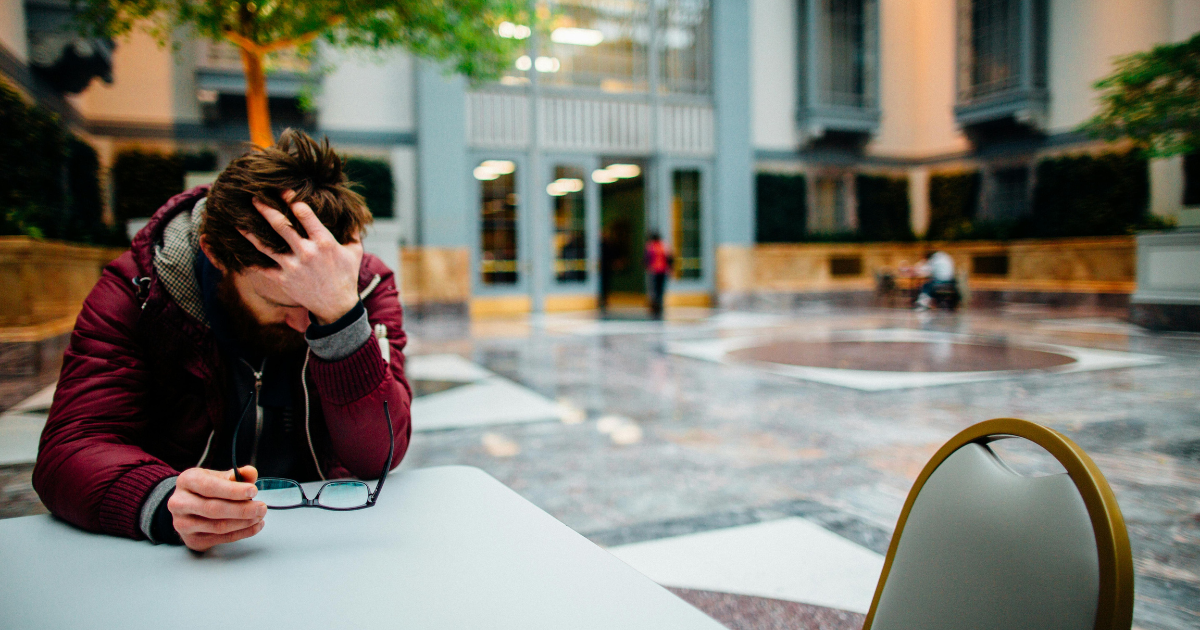 Stressed man with head in hand, glasses on table. Concept: stress, mortality, health, anxiety, mental health. 