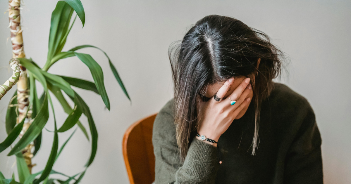 Woman with hand on forehead, potentially depicting bipolar disorder. Ketamine treatment concept. Plant on left.